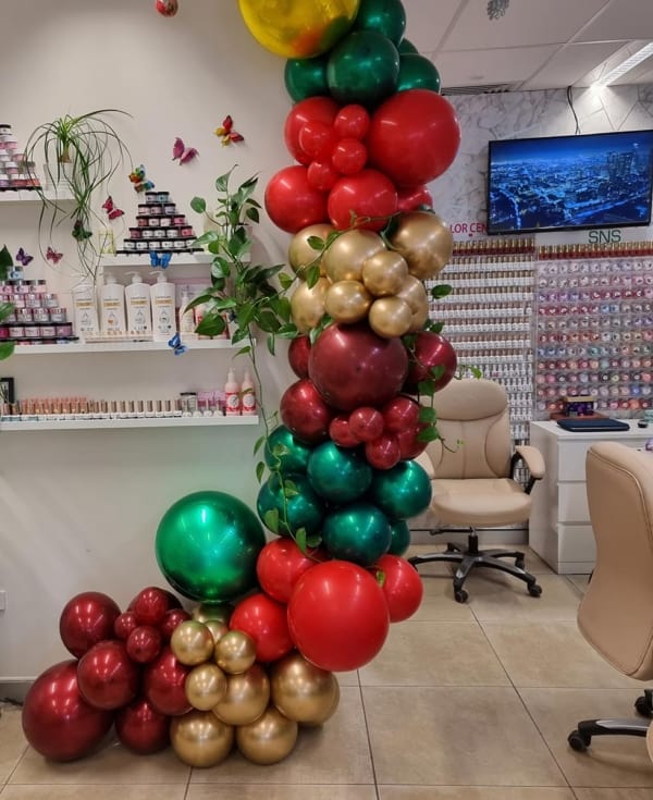 A red, green and gold balloon garland in Christmas colours at a Perth nail salon.