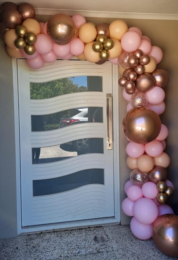 A pretty balloon garland in pink, blush, peach and gold hues above a doorway.