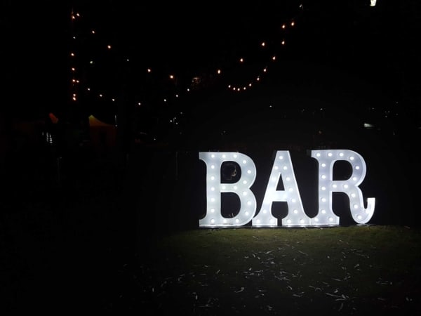 Bar light up letters under fairy lights on a lawn at night.