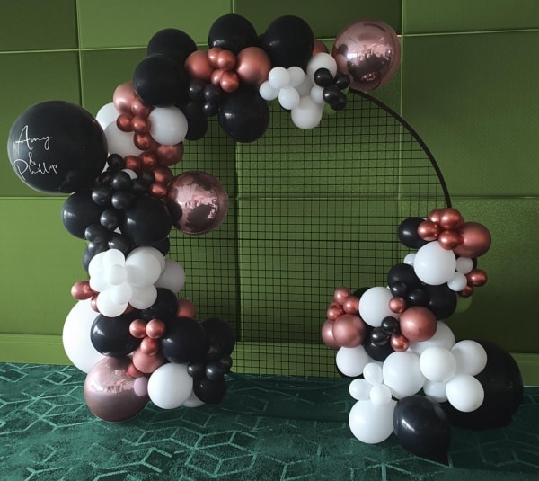 A personalised circular balloon garland in black, white & pink arranged on a black mesh frame.