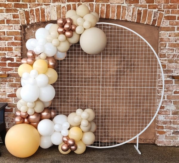 A balloon garland in white, sand, bronze and yellow hues arranged on a mesh frame.