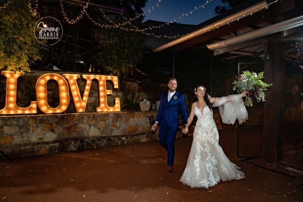 Bride and groom walking in front of giant light up LED love letters at their wedding.