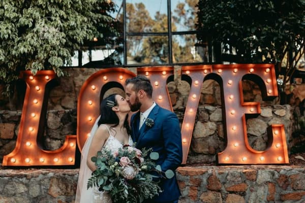 Bride and groom kissing in front of giant light up love letters at their wedding.