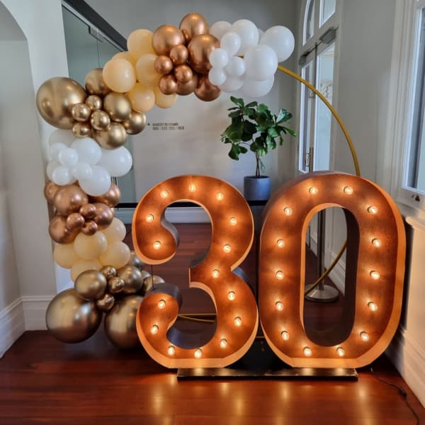 Giant number lights and a garland of gold balloons for a 30th birthday party.
