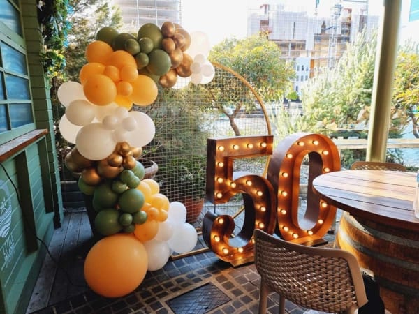 Giant rustic 50 number lights with green and yellow balloons on a verandah.