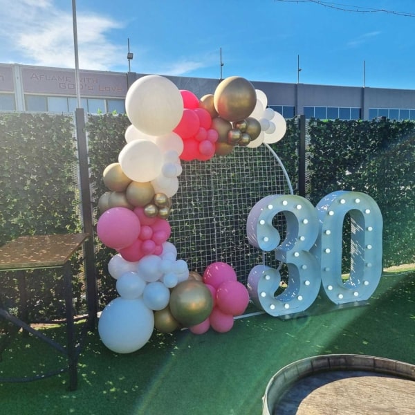 Giant white LED number lights with a pink, gold and white balloon garland.
