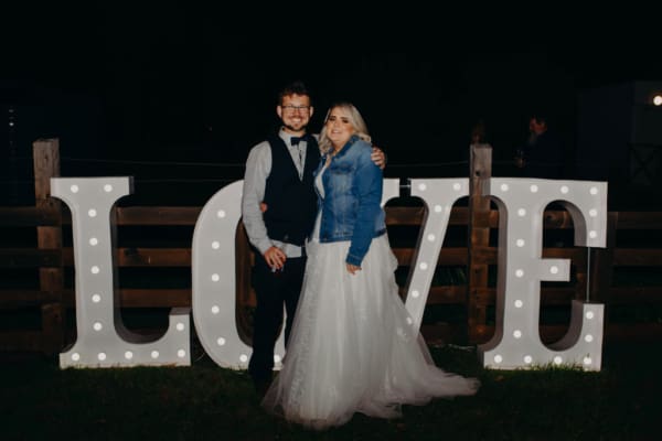 Bride and groom standing in front of giant light up love letters.