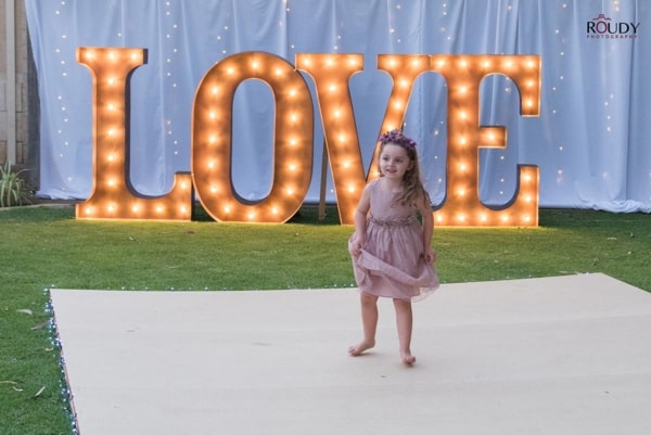 Giant golden light up letters at a wedding, with a flower girl on the dance floor.