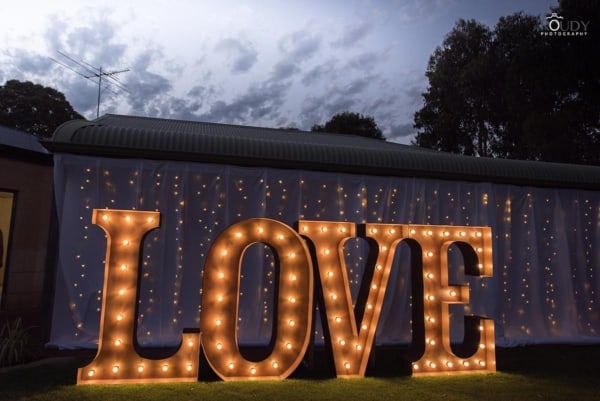 Giant golden light up letters at a wedding, with a sparkling fairy light backdrop.