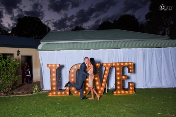 Couple kissing in front of giant golden light up letters at a wedding.