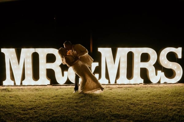 Bride and groom kissing in front of white MR & MRS light up letters.