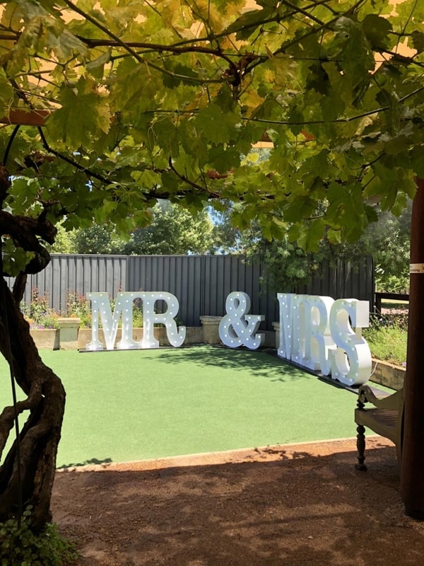 White LED MR & MRS light up letters under grapevines at a backyard wedding.