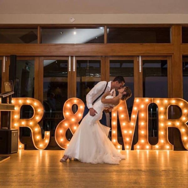 Bride and groom kissing on the dance floor with rustic gold light up MR & MRS letters in the background.