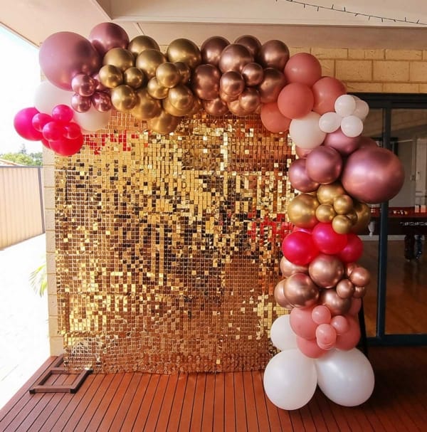 A golden shimmer wall with pink, gold and white balloons.