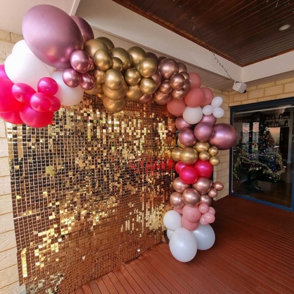 A golden shimmer wall with pink, gold and white balloons on a deck.